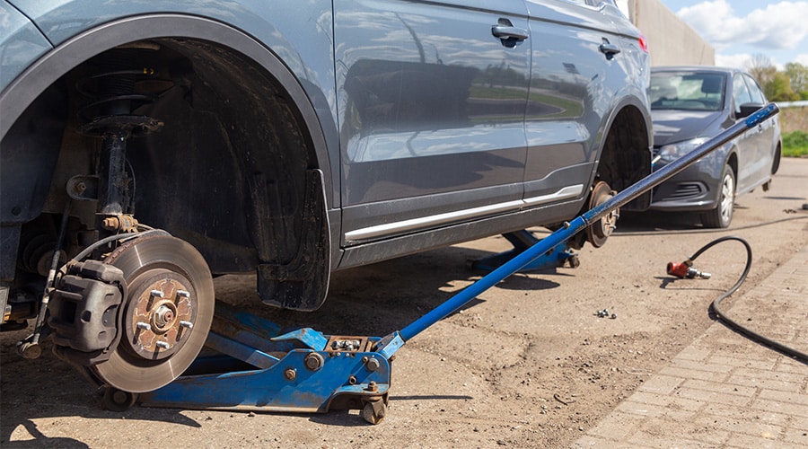 Pre-trip Inspection Checklist Before Your Summer Road Trip | Image of 2 cars on tire mounting with removed wheel on pneumatic jack, seasonal tire change, car service concept, Tire service, Seasonal change, A car without a wheel lifted on a jack.