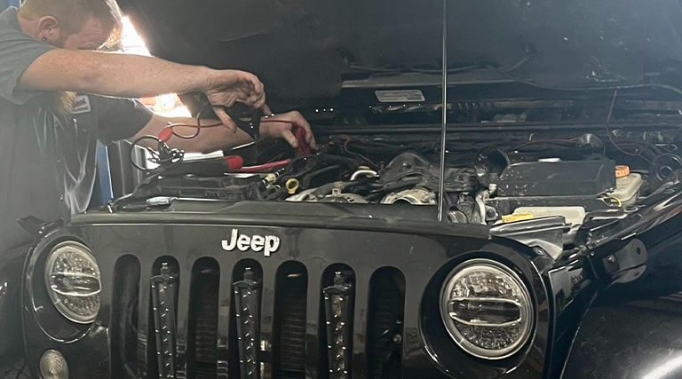 Holiday Road Trip Safety Checklist | Maxi Auto Repair Jacksonville. Mechanic at Maxi Auto Repair Hodges in Jacksonville, FL. tests battery in black jeep wrangler in shop.