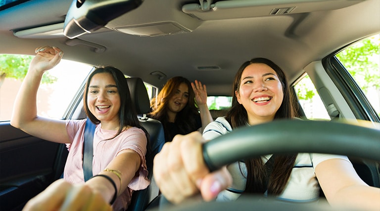 Holiday Travel Car Care Tips and Playlist | Maxi Auto Repair Jacksonville. Young women driving and singing while turning up music and driving.