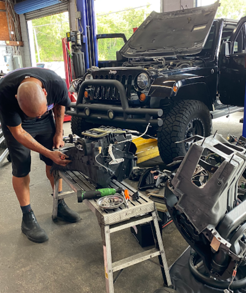 Expert Jeep Repair Services | Maxi Auto Repair Jacksonville, FL. Image of mechanic in shop repairing engine parts of a black jeep wrangler in shop.