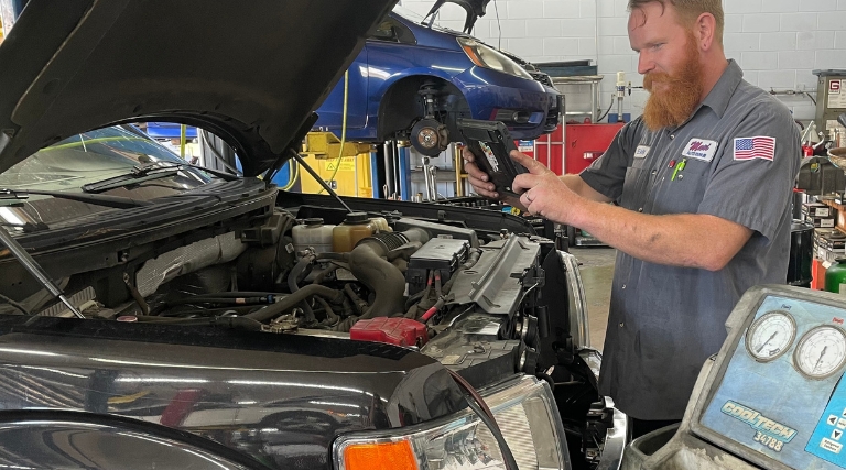 AC maintenance and repair near me in Jacksonville, FL at Maxi Auto Repair. Image of a technician inspecting the AC system under the open hood of a car using the Cool-Tech 34788 equipment.